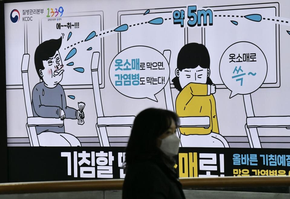 A woman wearing a face mask walks past a poster showing preventative measures against infectious diseases, at a railway station in Seoul on March 21, 2020. 